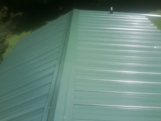 New green metal panels meeting at the ridge of a roof — Flat Roof Repair work by our crew in Spotsylvania