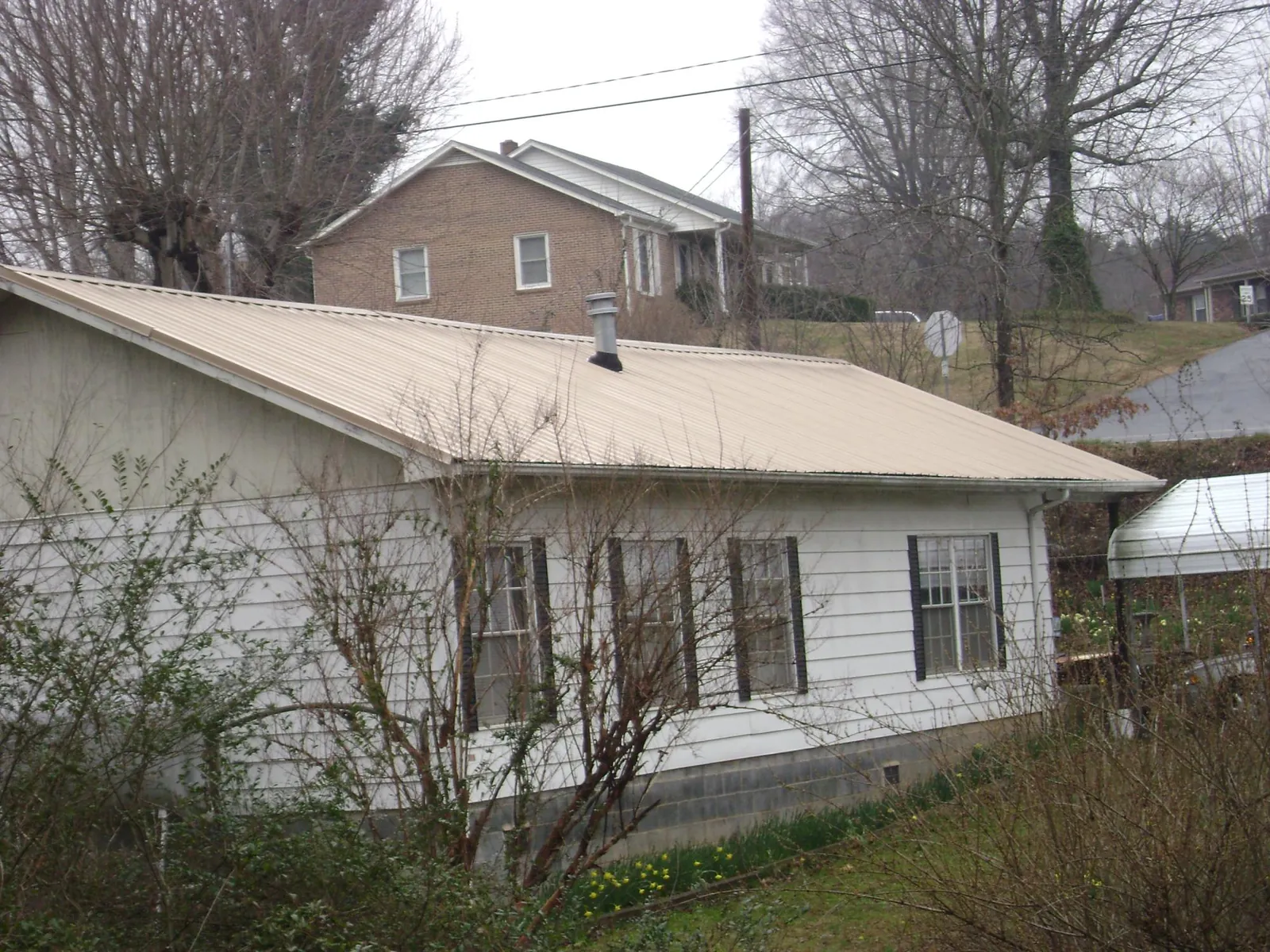 Tan metal roof on a white sided house set into a hillside — Commercial Roofing by Roofing Brothers in Spotsylvania